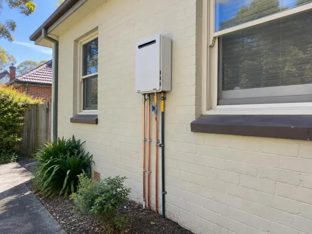 Exterior wall hot water unit with copper and insulated pipes beside house windows in Hornsby